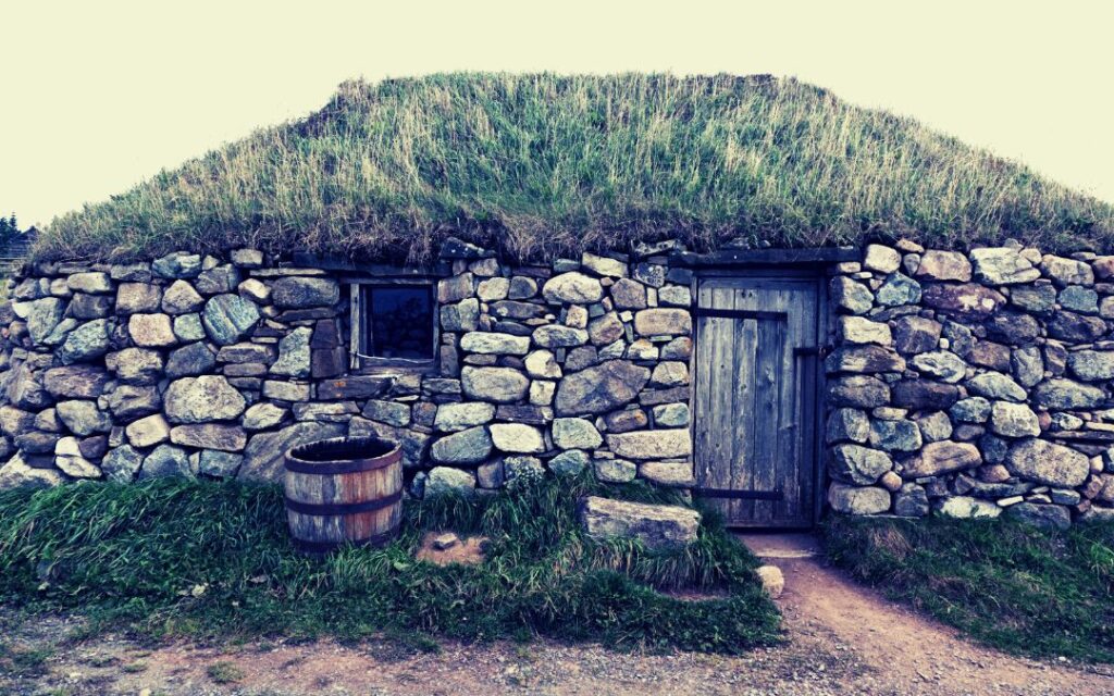 Stone building with wood door built into a hillside with grass roof illustrates Dark Academic Decor