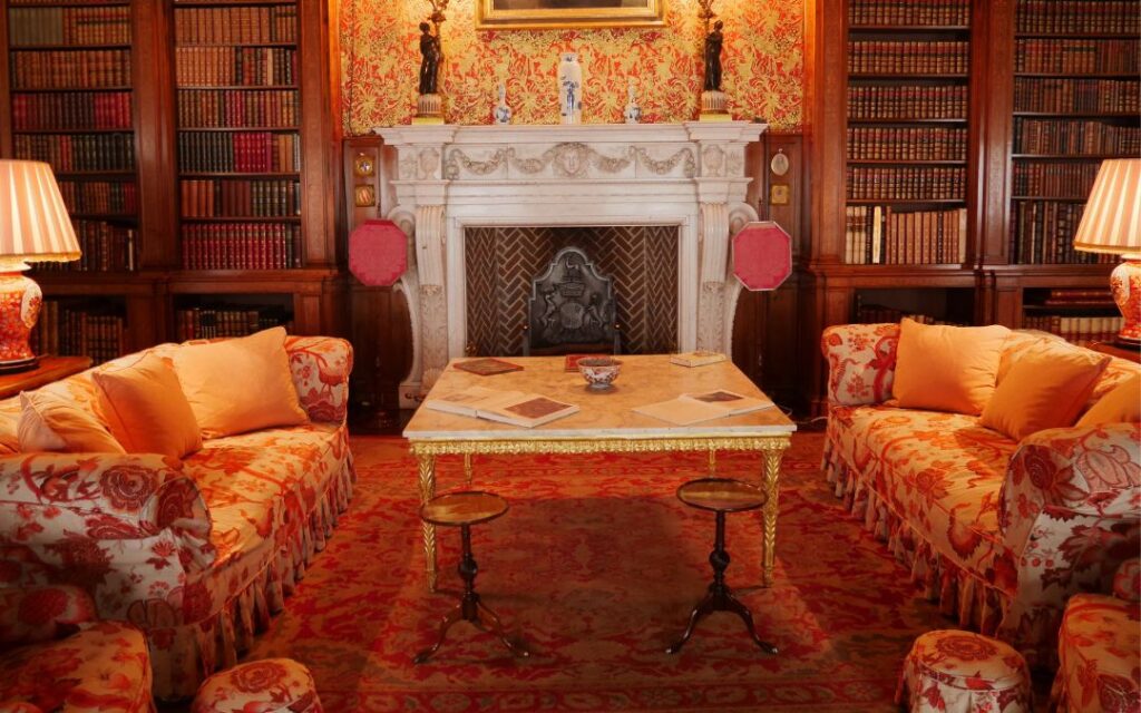 Luxurious living room with deep red silk couches and marble fireplace flanked by bookcases of antique leather books in the style of Dark Academia Decor